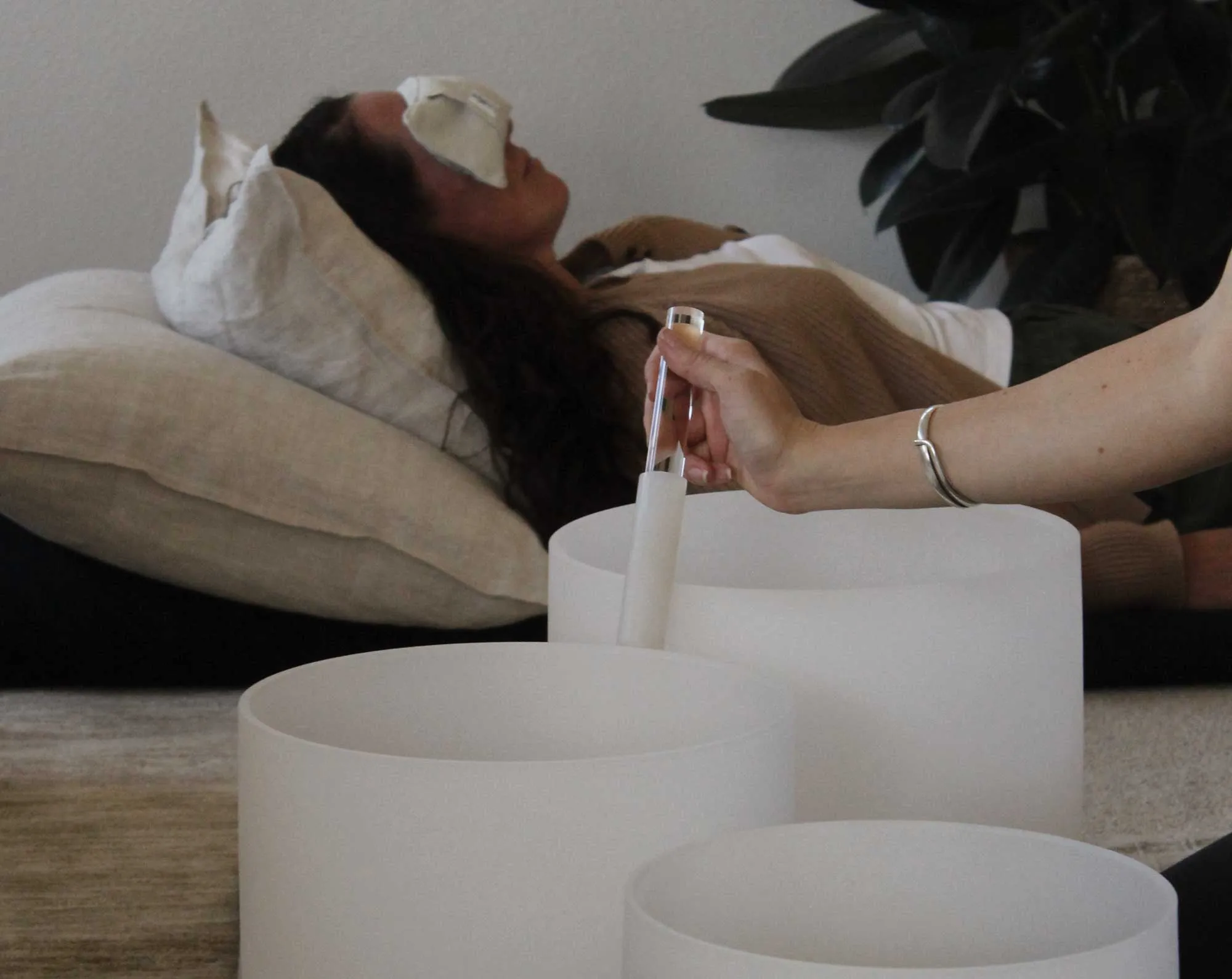 A client resting with an eye pillow while a frosted crystal singing bowl is played beside them